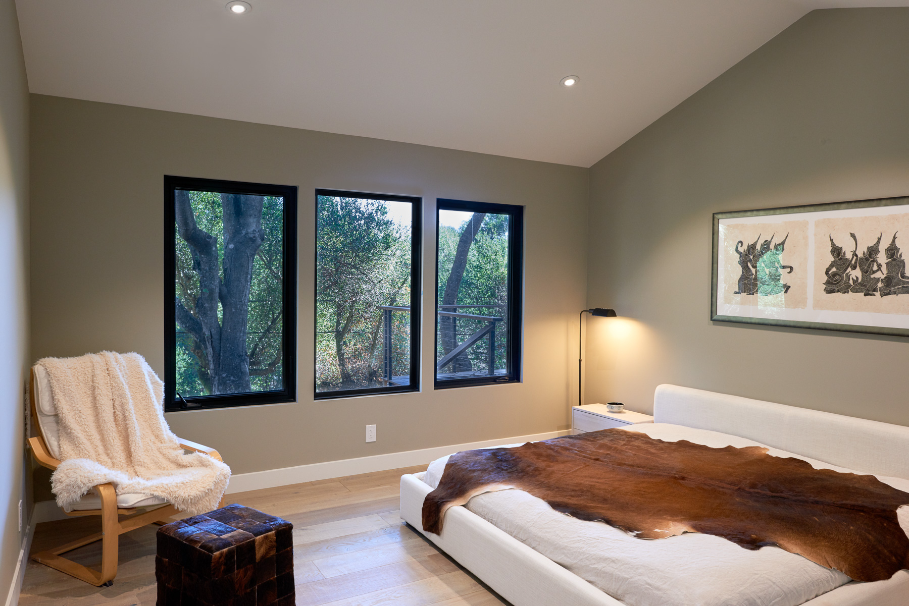 Serene bedroom with three framed windows looking onto trees