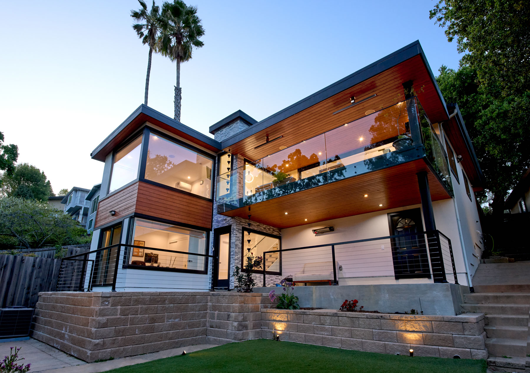 Modern hillside residence at dusk with warm interior light and glass railings